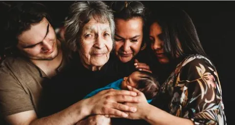 A group of three people with varying ages centred around an elderly woman holding a baby swaddled in blue.